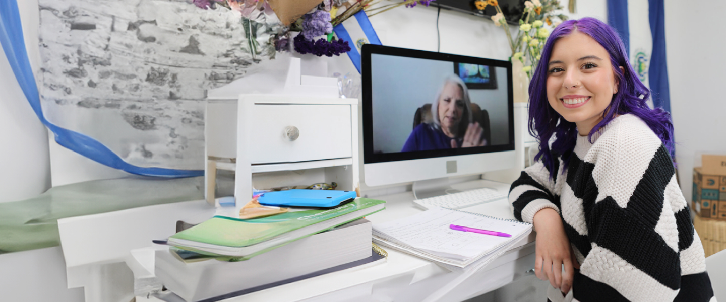 A woman with vibrant purple hair working at a desk with a computer.